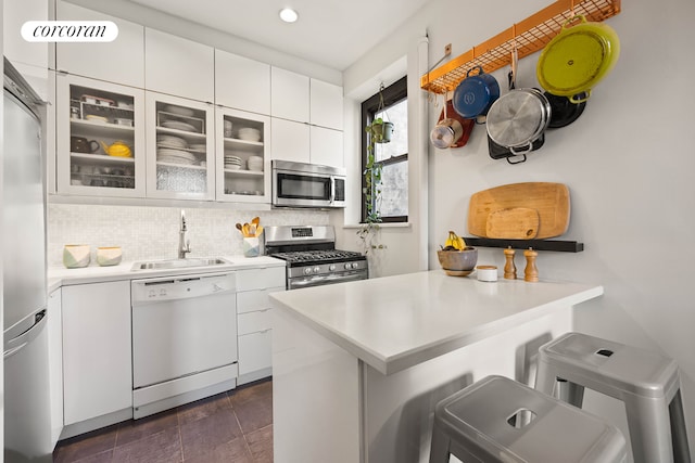 kitchen with stainless steel appliances, a sink, light countertops, white cabinets, and a peninsula