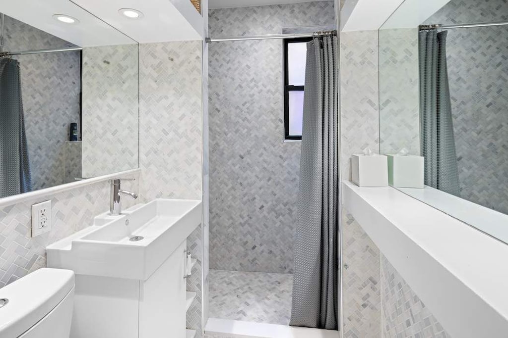 bathroom featuring tile walls, a tile shower, toilet, vanity, and recessed lighting