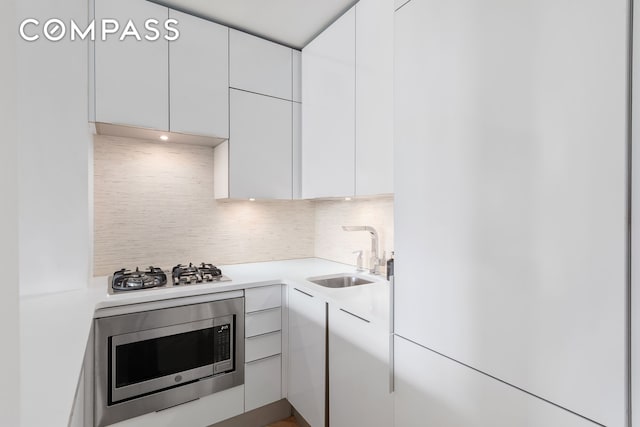 101 W 12th St Unit 12B, New York City, NY 10011 - kitchen featuring a sink, stainless steel microwave, white cabinetry, backsplash, and light countertops
