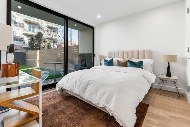 bedroom featuring access to outside, wood finished floors, a wall of windows, baseboards, and recessed lighting