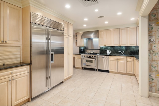 kitchen featuring high end appliances, wall chimney exhaust hood, backsplash, light brown cabinetry, and recessed lighting