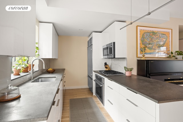 kitchen featuring modern cabinets, appliances with stainless steel finishes, a sink, white cabinets, and light wood-type flooring