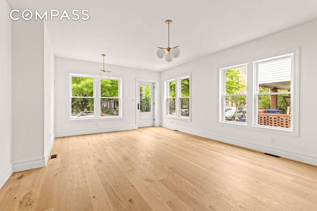 empty room with a chandelier, healthy amount of natural light, baseboards, and light wood-style flooring