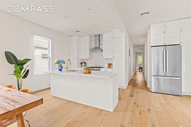 kitchen featuring stainless steel refrigerator, wall chimney range hood, light wood-style floors, light countertops, and recessed lighting