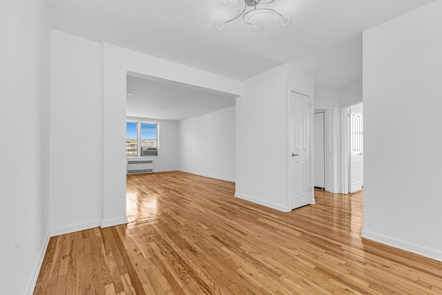 spare room with radiator heating unit, light wood-type flooring, baseboards, and a chandelier
