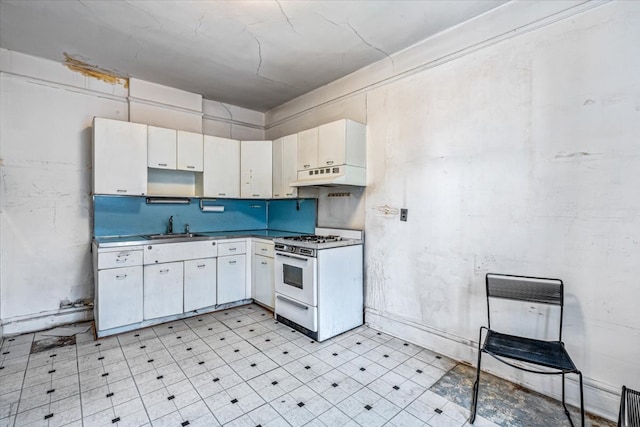 kitchen with white gas range, under cabinet range hood, a sink, light floors, and white cabinets