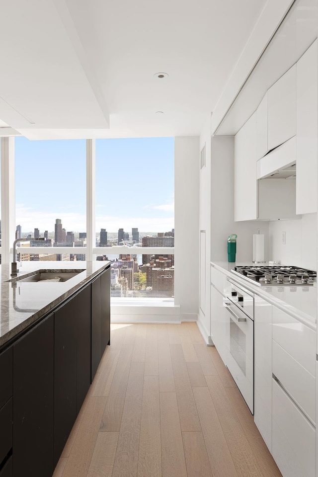 kitchen with oven, a sink, stainless steel gas stovetop, light wood finished floors, and white cabinetry