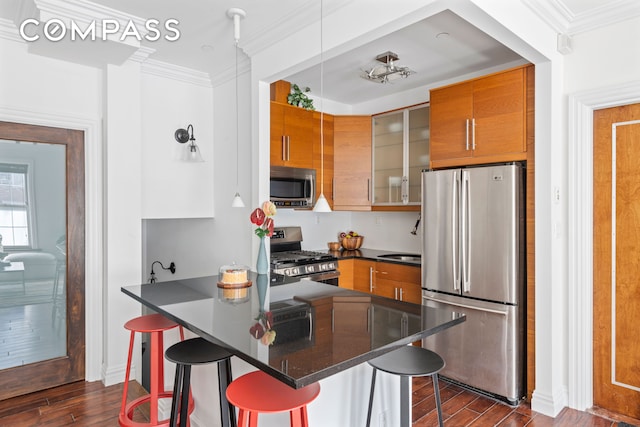 kitchen featuring stainless steel appliances, dark wood-type flooring, a breakfast bar area, dark countertops, and crown molding