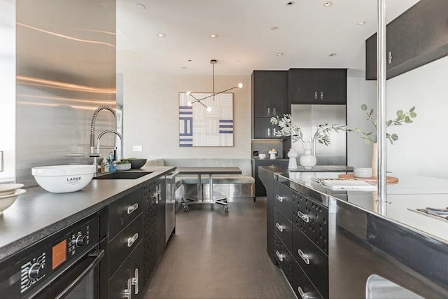 kitchen with dark cabinetry, stainless steel appliances, a sink, finished concrete flooring, and dark countertops