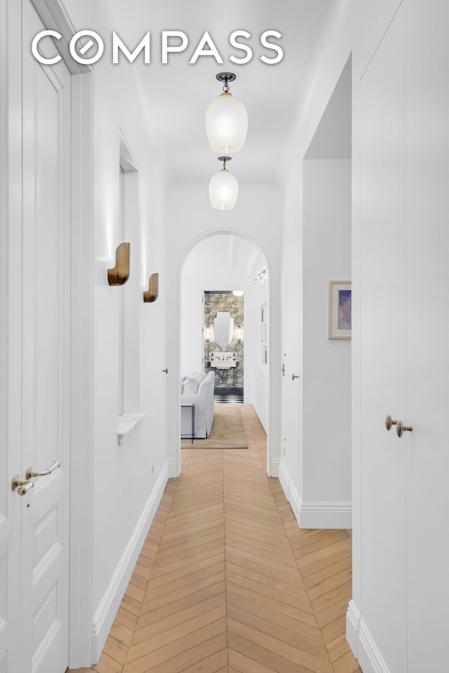 hall featuring arched walkways and baseboards