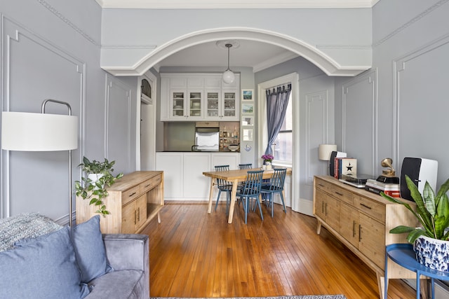 dining area with arched walkways, hardwood / wood-style flooring, ornamental molding, and a decorative wall