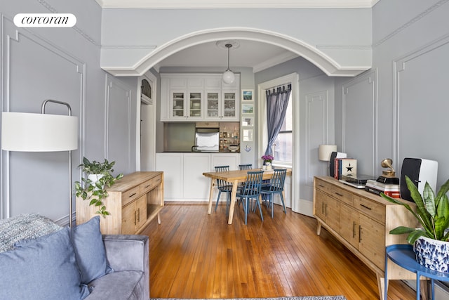 dining area featuring arched walkways, hardwood / wood-style flooring, and crown molding