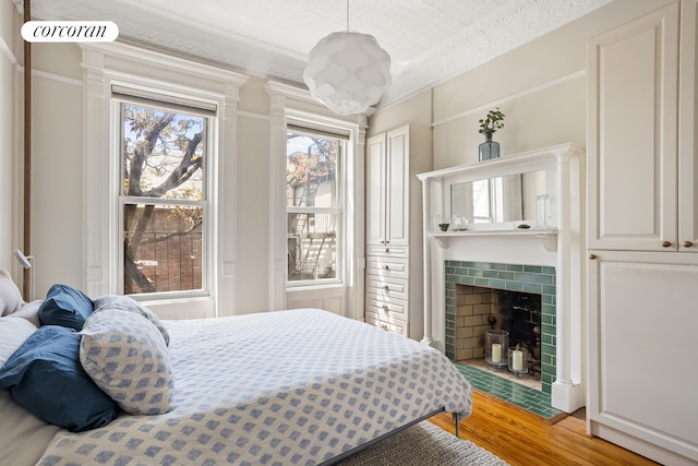 bedroom with light wood-style floors, a fireplace, and ornamental molding