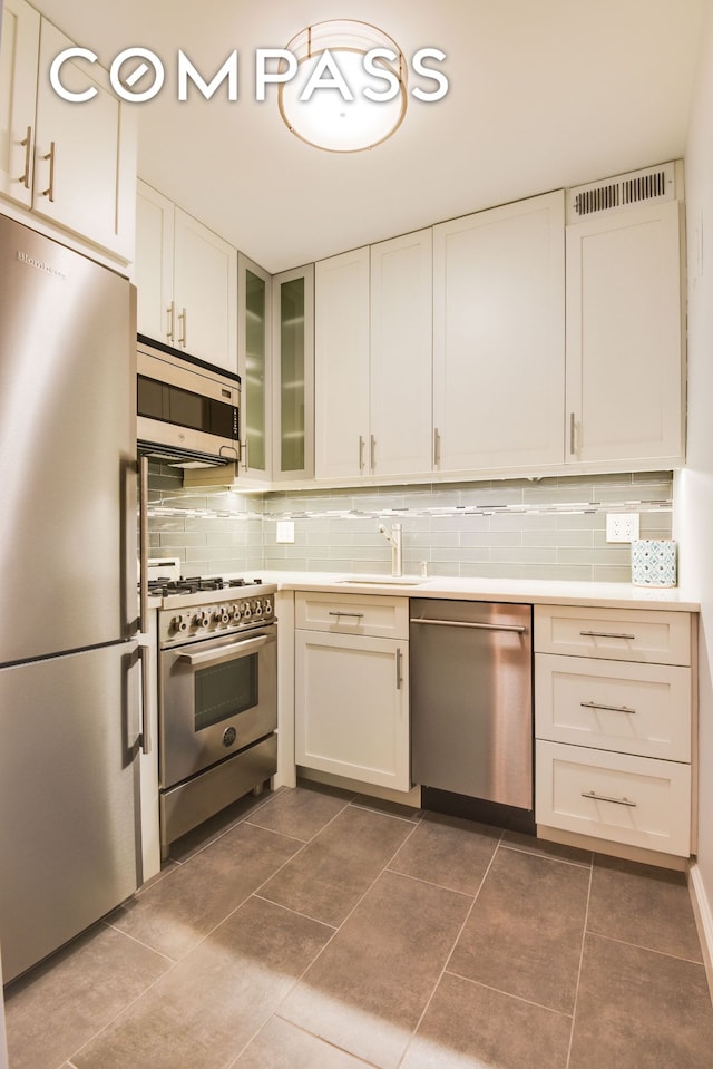 kitchen featuring appliances with stainless steel finishes, a sink, backsplash, white cabinets, and light countertops