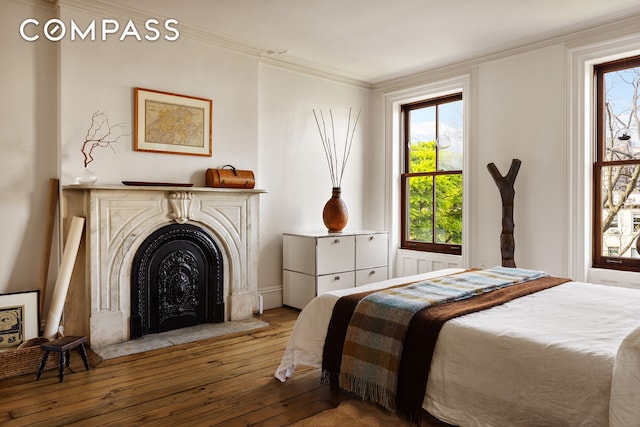 bedroom featuring hardwood / wood-style floors, ornamental molding, and a fireplace with flush hearth
