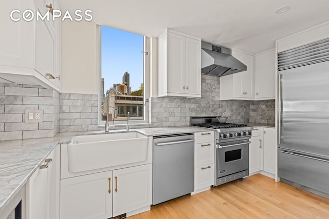 146-148 W 22nd St Ph, Ph, New York City, NY 10011 - kitchen featuring high quality appliances, range hood, white cabinetry, light stone countertops, and light wood-style floors