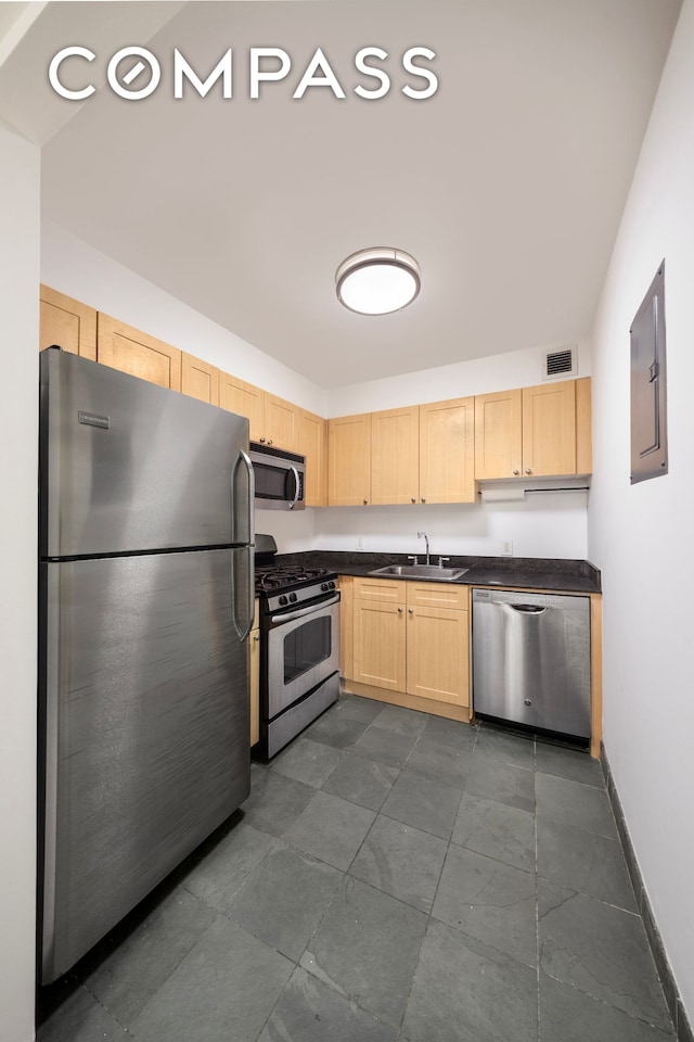 kitchen with stainless steel appliances, light brown cabinetry, dark countertops, a sink, and baseboards