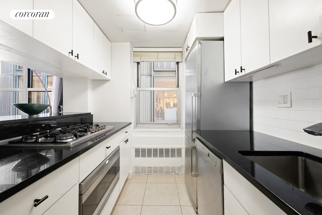 kitchen with stainless steel appliances, tasteful backsplash, white cabinetry, light tile patterned floors, and a sink