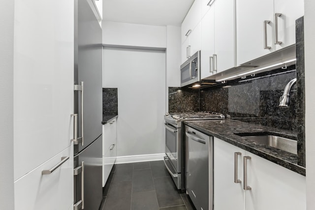 kitchen with stainless steel appliances, a sink, white cabinets, backsplash, and dark stone countertops