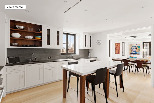 kitchen with a sink, backsplash, light wood-type flooring, and glass insert cabinets