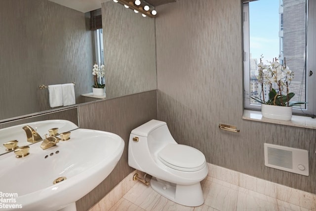 half bathroom with a sink, toilet, and wallpapered walls