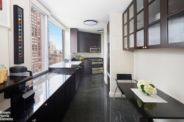kitchen featuring stainless steel appliances, granite tiled floors, a sink, glass insert cabinets, and baseboards