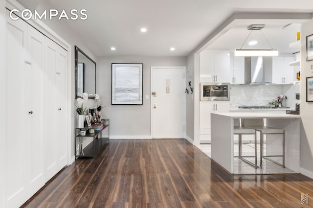 33-44 93rd St Unit 5X, New York City, NY 11372 - kitchen with wall chimney range hood, stainless steel microwave, white cabinets, tasteful backsplash, and dark wood finished floors
