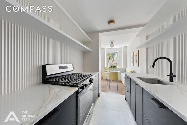 kitchen featuring stainless steel gas range oven, a sink, open shelves, light stone countertops, and light tile patterned flooring