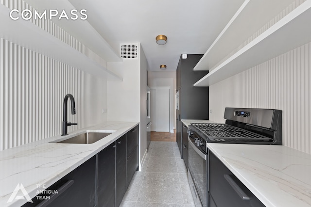 kitchen with stainless steel gas range, dark cabinets, open shelves, a sink, and baseboards