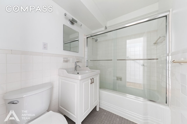 bathroom featuring tile walls, toilet, bath / shower combo with glass door, vanity, and tile patterned flooring