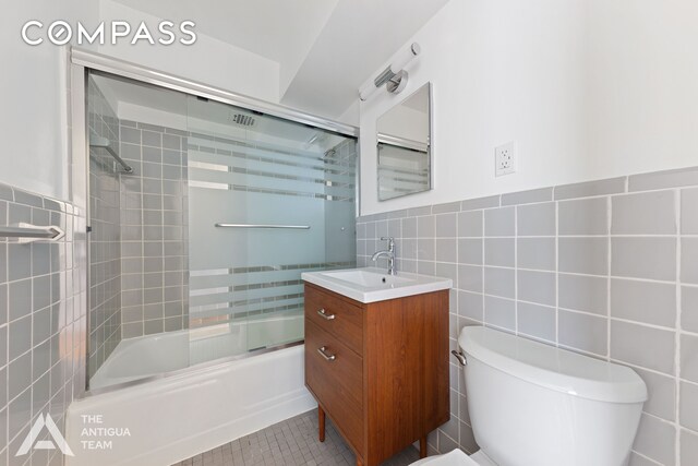 bathroom featuring tile walls, bath / shower combo with glass door, vanity, toilet, and tile patterned floors