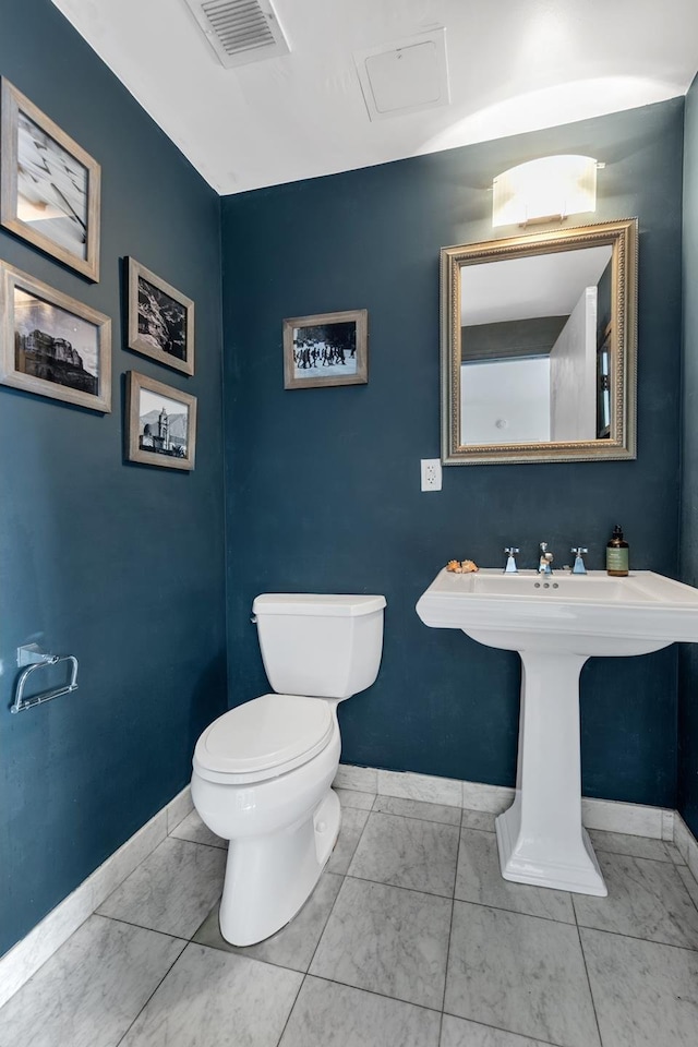 half bathroom featuring baseboards, marble look tiles, and toilet