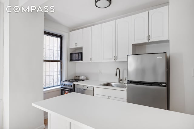 kitchen with stainless steel appliances, a sink, light countertops, and white cabinets