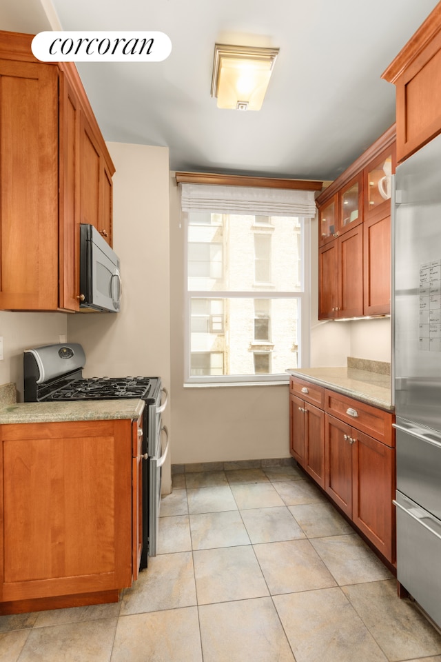 kitchen with stainless steel appliances, brown cabinets, glass insert cabinets, and light stone counters