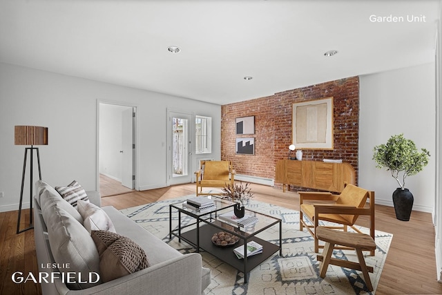 living area featuring baseboards, light wood-type flooring, and brick wall