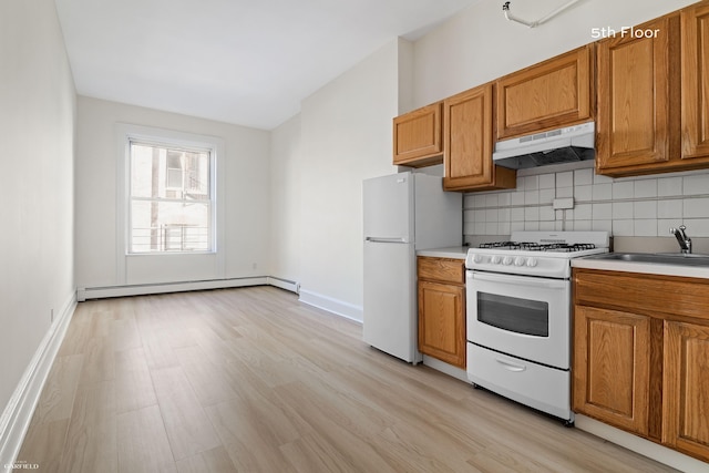 kitchen with under cabinet range hood, white appliances, baseboard heating, a sink, and tasteful backsplash