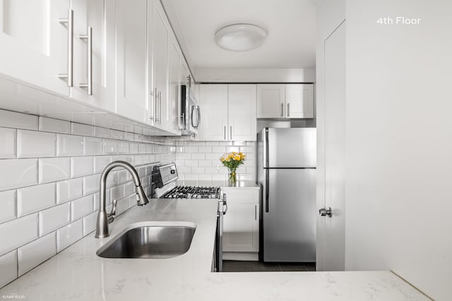kitchen with stainless steel appliances, a sink, white cabinets, tasteful backsplash, and light stone countertops