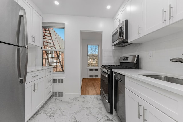 kitchen with stainless steel appliances, radiator, decorative backsplash, white cabinetry, and recessed lighting