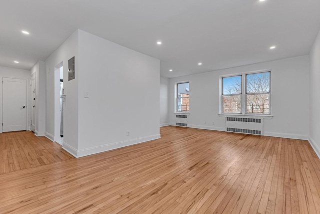 empty room featuring radiator, light wood-style floors, baseboards, and recessed lighting