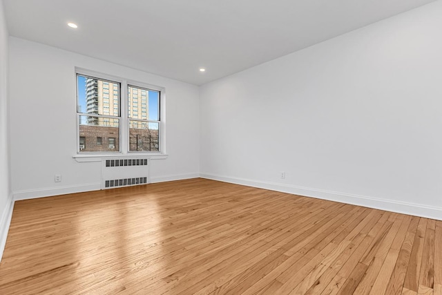 unfurnished room featuring radiator, light wood finished floors, baseboards, and recessed lighting