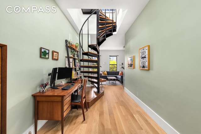 office with light wood-style floors, a high ceiling, and baseboards