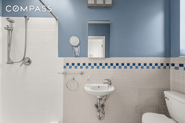 bathroom with tiled shower, toilet, tile walls, wainscoting, and a sink