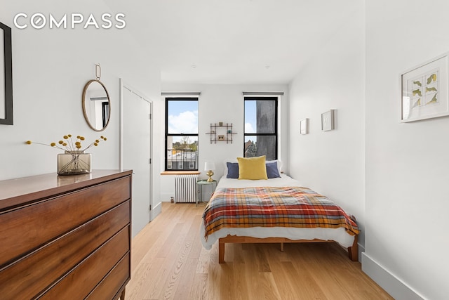 bedroom featuring radiator, light wood-style floors, and baseboards