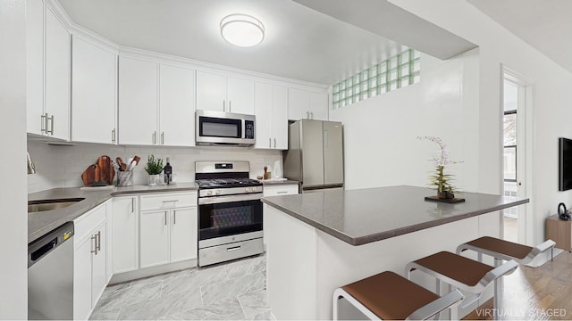 599 E 7th St Unit 2B, New York City, NY 11218 - kitchen with stainless steel appliances, a breakfast bar area, decorative backsplash, and white cabinetry