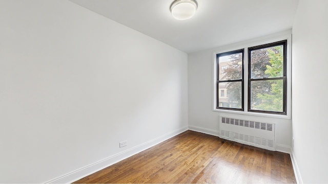 unfurnished room with radiator heating unit, baseboards, and wood finished floors