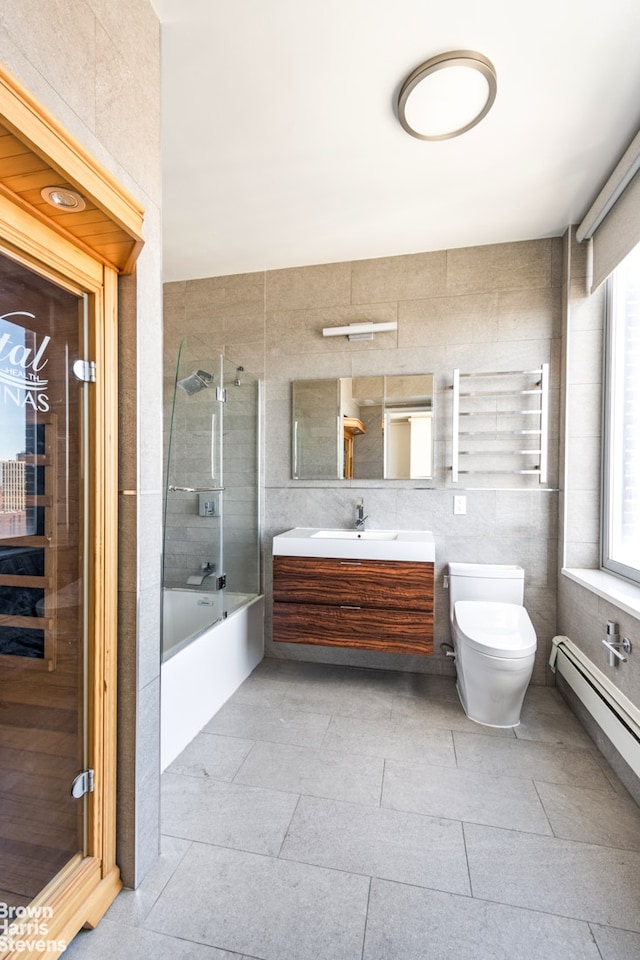 full bath featuring baseboard heating, toilet, vanity, combined bath / shower with glass door, and tile walls