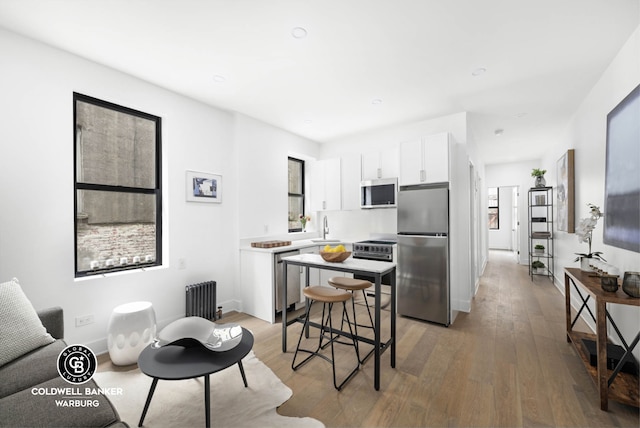 kitchen with stainless steel appliances, white cabinetry, a sink, light wood finished floors, and a kitchen island