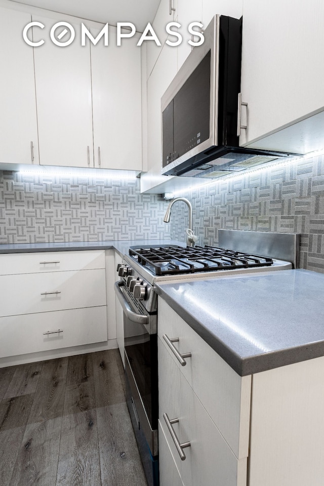 kitchen with appliances with stainless steel finishes, dark wood-style flooring, white cabinets, and backsplash