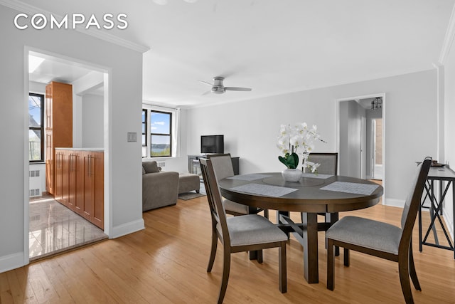 dining space featuring light wood-style flooring, baseboards, a ceiling fan, ornamental molding, and radiator heating unit