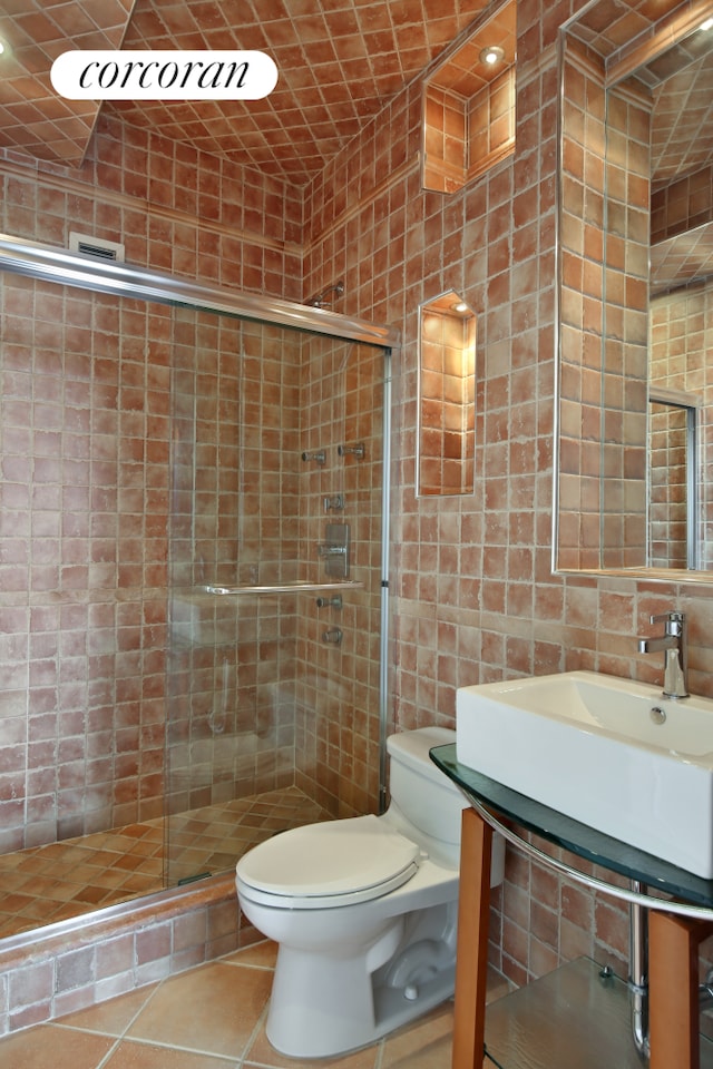 bathroom featuring a shower stall, toilet, tile patterned floors, tile walls, and a sink